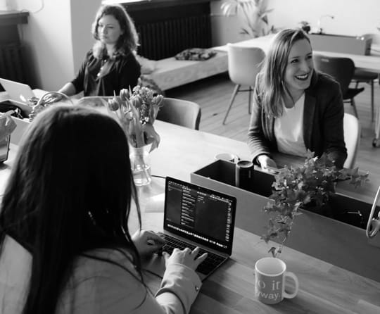 girls sitted around a table using laptops.