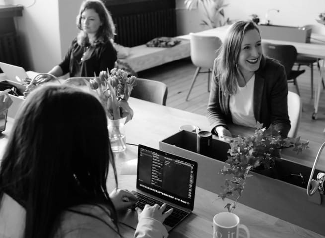 girls sitted around a table using laptops.